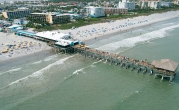 drone-video:-surfers,-beachgoers-at-cocoa-beach-pier,-great-place-to-watch-rocket-launch